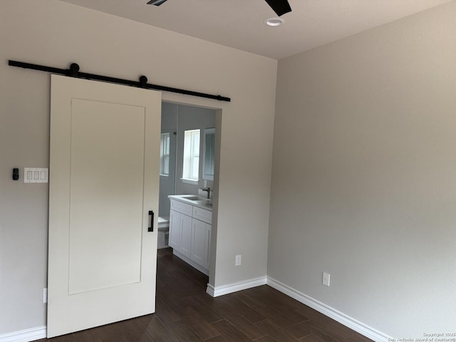 unfurnished bedroom featuring a barn door, baseboards, dark wood-type flooring, and a sink