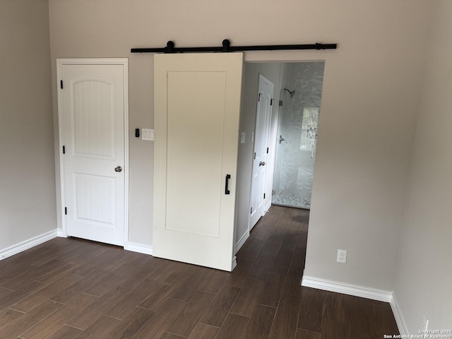 unfurnished bedroom with wood finish floors, baseboards, and a barn door