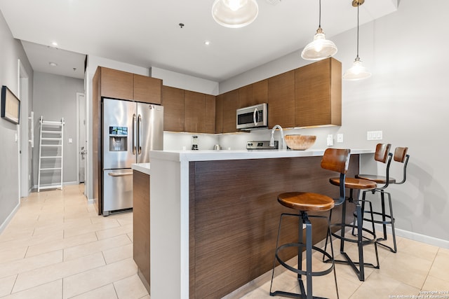 kitchen with a kitchen breakfast bar, pendant lighting, appliances with stainless steel finishes, light tile patterned floors, and kitchen peninsula