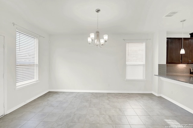 unfurnished dining area featuring light tile patterned flooring, plenty of natural light, and an inviting chandelier