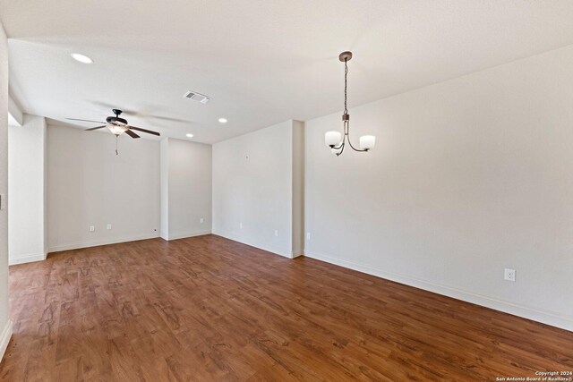 spare room featuring baseboards, visible vents, wood finished floors, and ceiling fan with notable chandelier