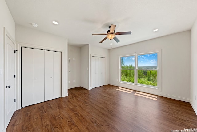 unfurnished bedroom with ceiling fan, dark hardwood / wood-style flooring, and two closets