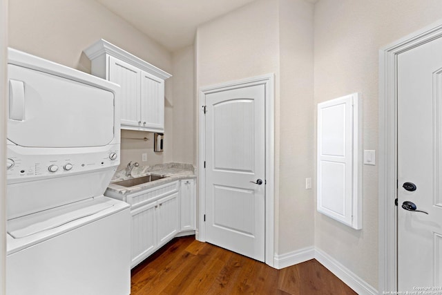 clothes washing area featuring stacked washer and dryer, dark wood-style flooring, a sink, baseboards, and cabinet space