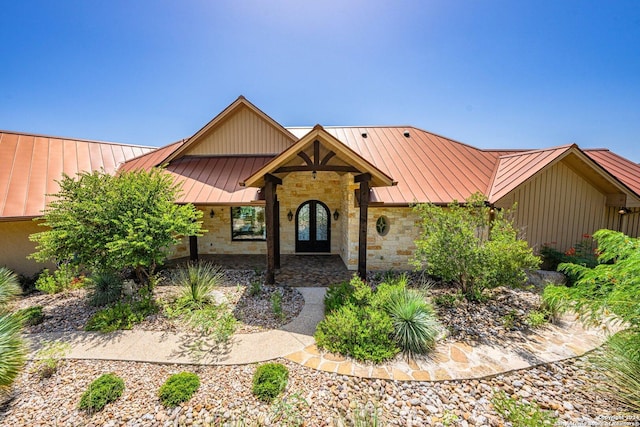 view of front of home featuring a standing seam roof, stone siding, metal roof, and french doors