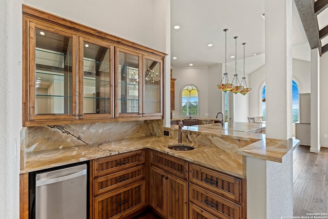 kitchen featuring stainless steel dishwasher, light stone countertops, pendant lighting, kitchen peninsula, and hardwood / wood-style flooring