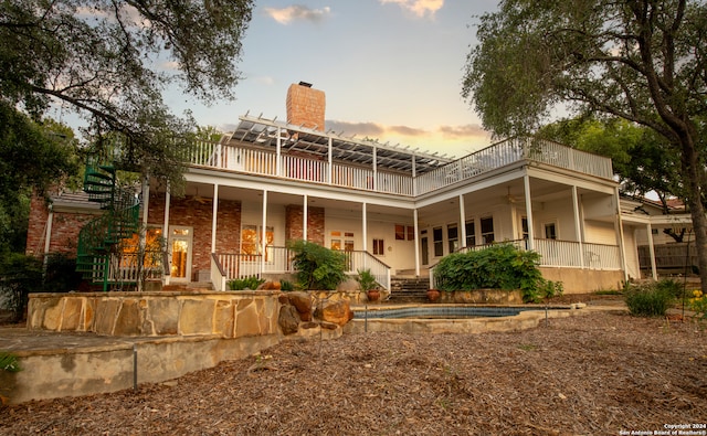 back house at dusk featuring a balcony and a porch