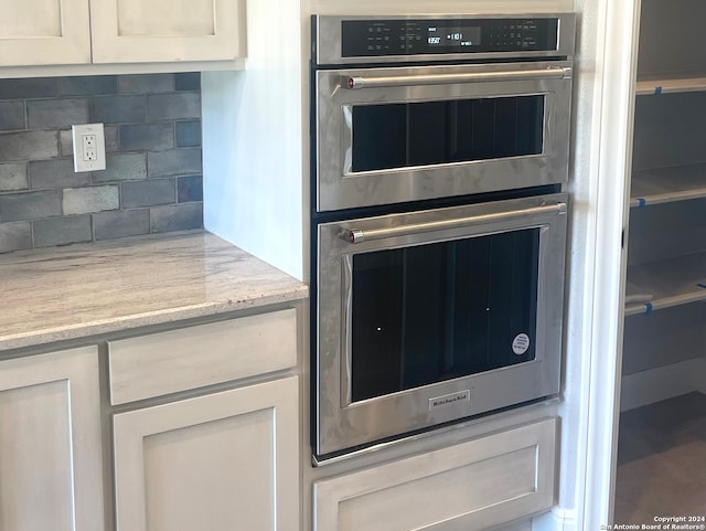 kitchen featuring decorative backsplash, light stone countertops, double oven, and white cabinetry