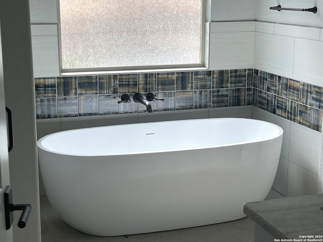 bathroom featuring plenty of natural light, a tub, and tile walls