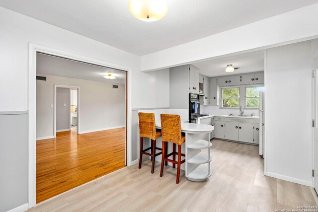 kitchen with black double oven, kitchen peninsula, white refrigerator, light hardwood / wood-style floors, and a breakfast bar