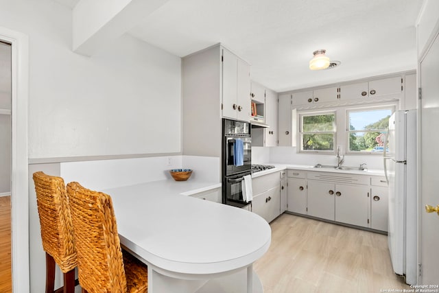 kitchen with black double oven, white refrigerator, light wood-type flooring, sink, and kitchen peninsula