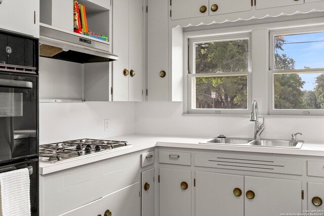 kitchen with backsplash, sink, stainless steel gas stovetop, and white cabinetry