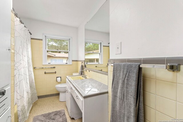 bathroom featuring toilet, tile patterned flooring, tile walls, vanity, and decorative backsplash