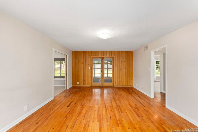 spare room with wood walls, a healthy amount of sunlight, and light hardwood / wood-style floors