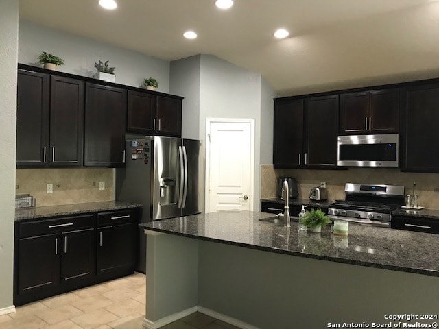 kitchen featuring sink, appliances with stainless steel finishes, a kitchen island with sink, and dark stone counters