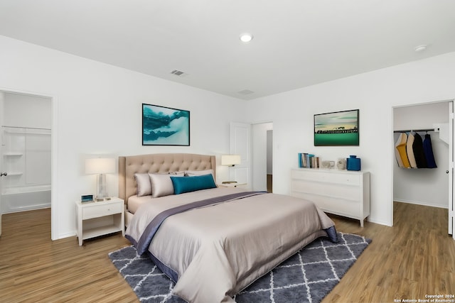 bedroom featuring a spacious closet, wood finished floors, visible vents, and baseboards