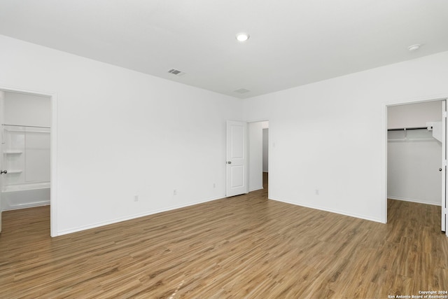 unfurnished bedroom featuring light wood finished floors, a closet, a walk in closet, and baseboards