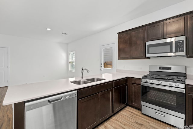 kitchen with appliances with stainless steel finishes, a peninsula, light countertops, dark brown cabinets, and a sink