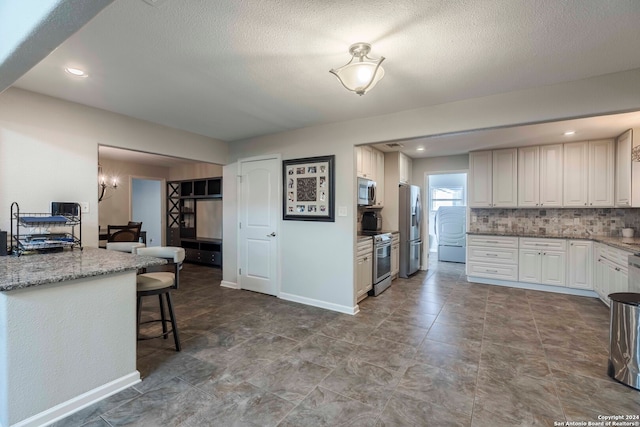 kitchen featuring dark tile patterned floors, appliances with stainless steel finishes, tasteful backsplash, light stone counters, and white cabinets