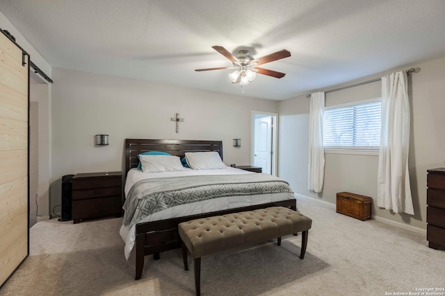 carpeted bedroom with a barn door, ceiling fan, and a textured ceiling