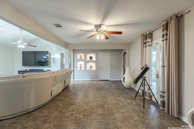 unfurnished living room with ceiling fan, dark tile patterned floors, and a textured ceiling