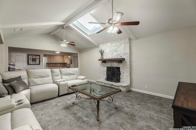 living room with beamed ceiling, tile patterned floors, a skylight, ceiling fan, and a stone fireplace