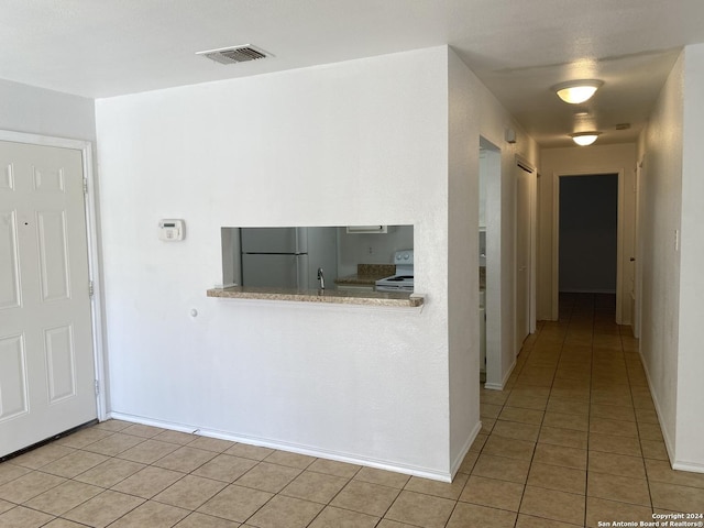 hallway featuring light tile patterned floors, visible vents, baseboards, and a sink