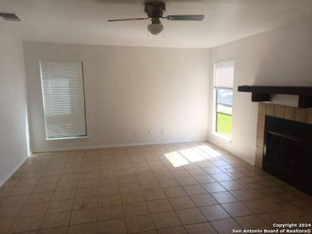 unfurnished living room with ceiling fan, light tile patterned floors, and a tiled fireplace