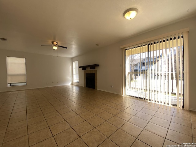 unfurnished living room featuring a ceiling fan, light tile patterned floors, a fireplace, and a wealth of natural light