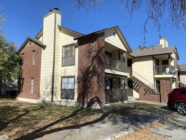 view of side of home with stairway, brick siding, and a chimney