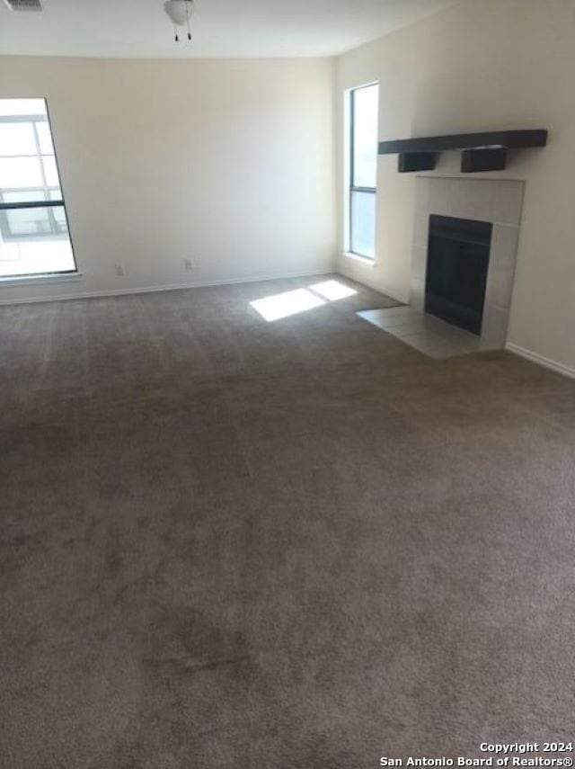 unfurnished living room featuring plenty of natural light, ceiling fan, carpet floors, and a tile fireplace