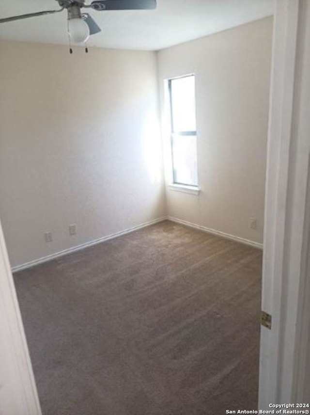 spare room featuring ceiling fan and dark colored carpet