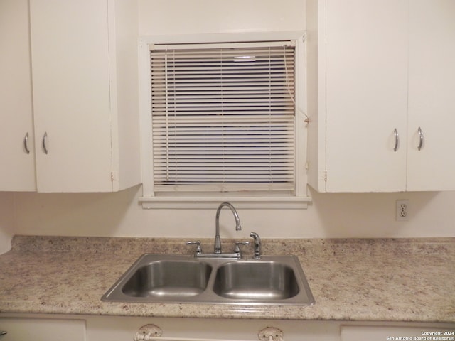 interior details with sink, light stone counters, and white cabinetry