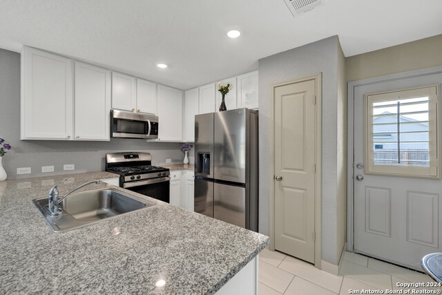 kitchen with appliances with stainless steel finishes, light stone counters, white cabinets, light tile patterned floors, and sink