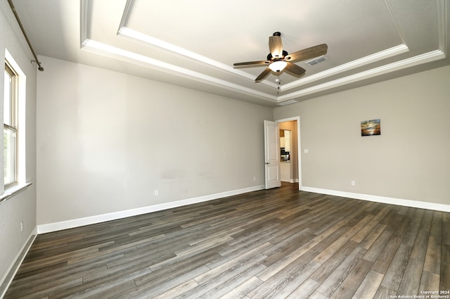 empty room featuring a raised ceiling, ceiling fan, dark wood-type flooring, and ornamental molding