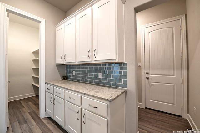 kitchen with white cabinetry, backsplash, light stone countertops, and dark hardwood / wood-style flooring