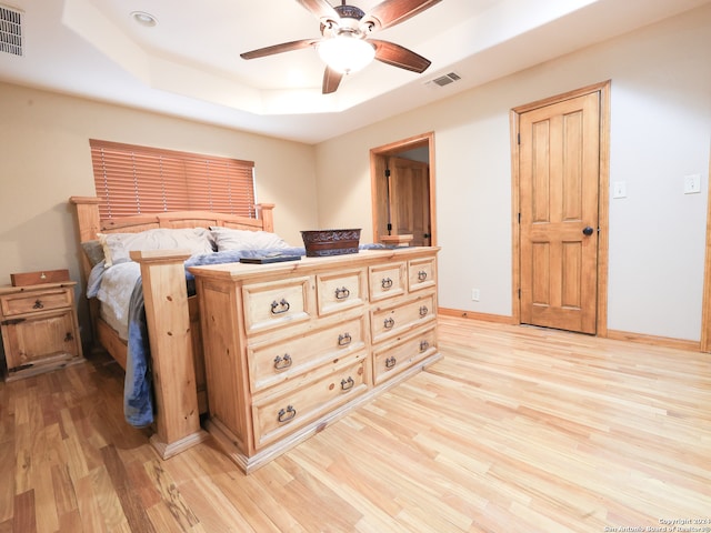 bedroom with ceiling fan, light wood-type flooring, and a raised ceiling