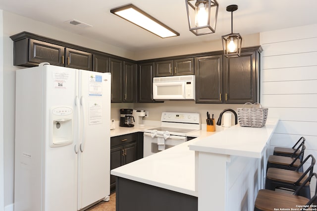 kitchen featuring pendant lighting, a breakfast bar, kitchen peninsula, white appliances, and dark brown cabinets