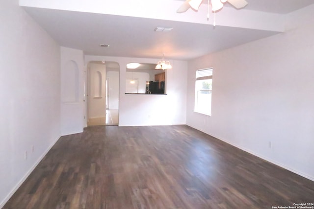 unfurnished living room with ceiling fan with notable chandelier and dark wood-type flooring