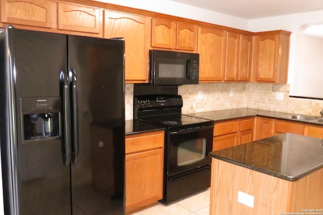 kitchen with light tile patterned floors, decorative backsplash, a sink, dark stone countertops, and black appliances