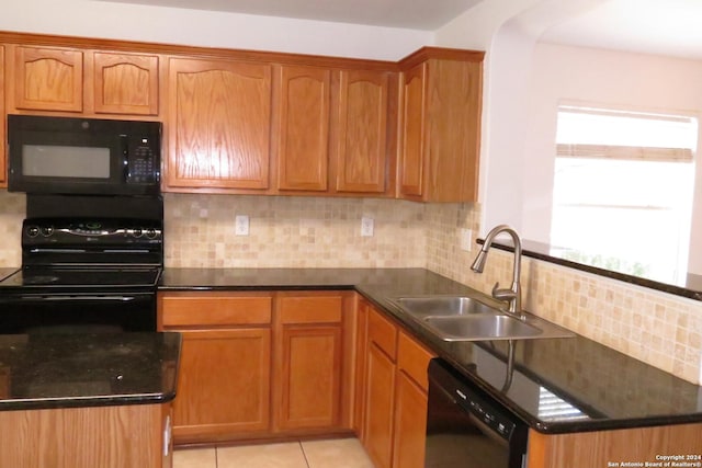 kitchen featuring dark countertops, a sink, black appliances, backsplash, and light tile patterned flooring