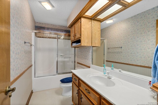 bathroom with wainscoting, shower / bath combination with glass door, a textured ceiling, and wallpapered walls