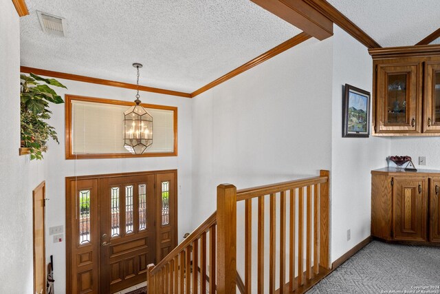 foyer entrance with a notable chandelier, visible vents, ornamental molding, light carpet, and a textured ceiling