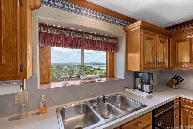 kitchen featuring a sink, light countertops, dishwasher, brown cabinetry, and wallpapered walls