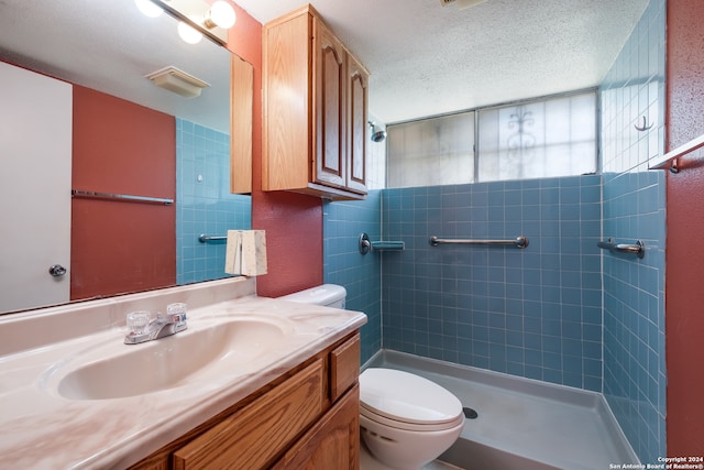 bathroom with vanity, a textured ceiling, toilet, and tiled shower