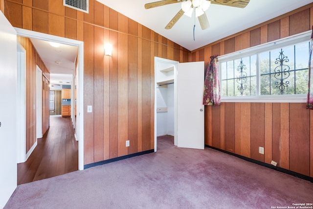 unfurnished bedroom featuring ceiling fan, wooden walls, carpet floors, and a spacious closet