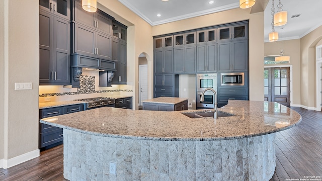 kitchen featuring hanging light fixtures, appliances with stainless steel finishes, a center island with sink, tasteful backsplash, and light stone counters