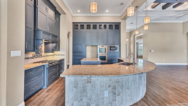 kitchen featuring a center island with sink, light stone counters, sink, dark wood-type flooring, and decorative light fixtures