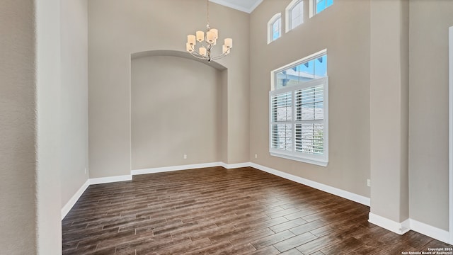 empty room featuring a chandelier, ornamental molding, hardwood / wood-style flooring, and a high ceiling