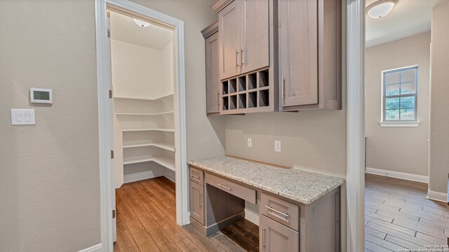 interior space featuring built in desk, wood-type flooring, and light stone counters