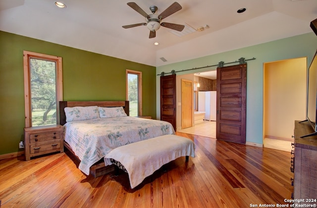 bedroom featuring ceiling fan, a barn door, light hardwood / wood-style flooring, connected bathroom, and lofted ceiling